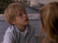 a young boy with glasses talking to another person