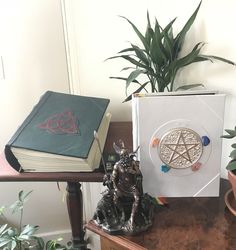 a table topped with books and a statue next to a potted plant on top of it