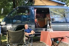 a man sitting at a table in front of a camper van with the door open