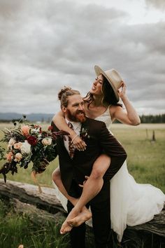 a bride and groom are sitting on a log in the grass with their arms around each other