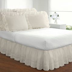 a bed with white ruffled bedspread and pillows on it in a room