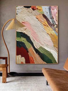 an abstract painting hangs on the wall next to a chair and lamp in a living room