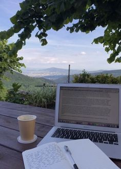 an open laptop computer sitting on top of a wooden table next to a cup of coffee