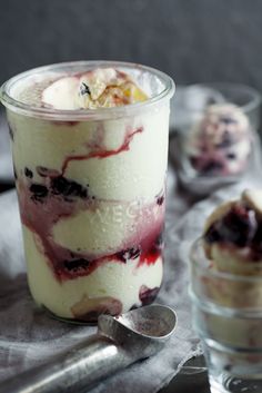 a dessert in a glass with ice cream and fruit toppings next to two spoons