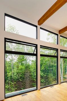 an empty room with large windows and wooden floors in front of trees outside the window