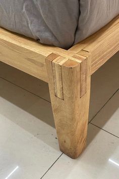 a wooden bed frame sitting on top of a white tile floor next to a pillow