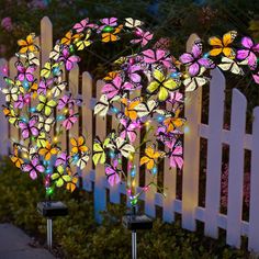 two solar powered butterfly lights in front of a white picket fence with pink and yellow butterflies