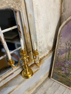 two candles are next to a painting on the window sill in an old house