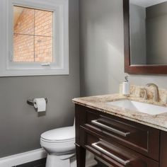 a white toilet sitting next to a bathroom sink under a mirror on top of a wooden cabinet