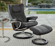 a black leather reclining chair and foot stool next to a glass table with a drink on it