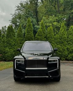 the front end of a black rolls royce parked in a driveway next to some trees