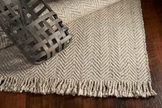 a metal basket sitting on top of a wooden floor next to a white and gray rug