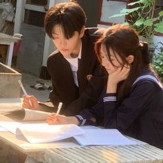 two people sitting at a table writing on paper