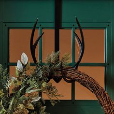 a wreath with antlers and greenery hanging from the front door to make it look like an antler's head