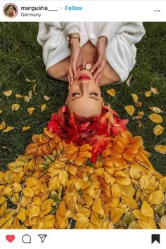 a woman laying on the ground surrounded by yellow and red leaves with her eyes closed