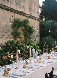 a long table set up with plates and flowers in front of an old stone building