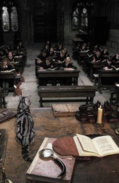 a room full of people sitting at desks with books on the floor and one person standing in front of them