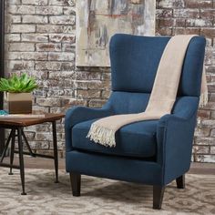 a blue chair with a blanket on it in front of a brick wall