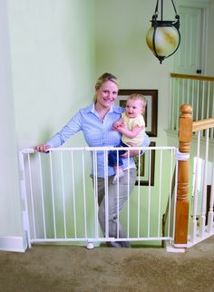 a woman holding a baby in her arms while standing next to a white gate with a wooden post