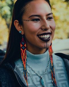 a woman with long necklaces and piercings on her face smiles at the camera