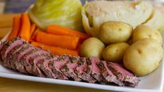 a white plate topped with meat, potatoes and carrots on top of a wooden table