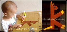 a toddler playing with construction paper and glue on a wooden table next to a cardboard cutout of a bird