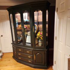 a china cabinet with glass doors and flowers in the bottom drawer, on top of a hard wood floor