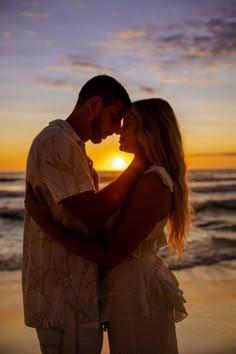 a man and woman standing next to each other on the beach at sunset with the sun setting behind them