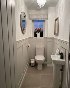 a white toilet sitting next to a sink in a bathroom under a window with a chandelier