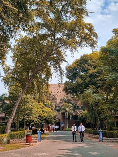 two people walking down the street in front of a building with trees on both sides