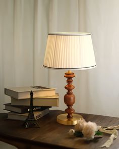 a lamp sitting on top of a wooden table next to a stack of books and a flower