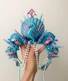 a hand holding up a blue and pink hair piece with pearls on the sides, two seahorses attached to it