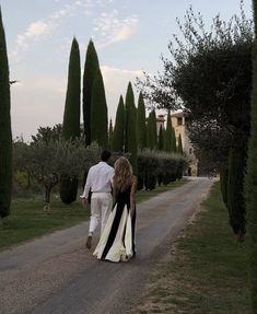 a man and woman walking down a road with trees in the background on either side