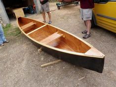 two men standing next to a small wooden boat on the ground with another man looking at it