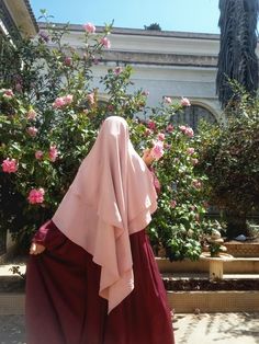 a woman in a pink and red dress walking by some flowers