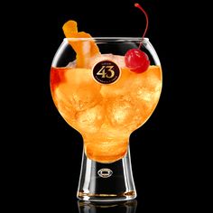 a glass filled with an orange liquid and topped with a cherry garnish, sitting on a black surface