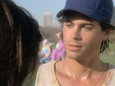 a young man wearing a baseball cap and looking at another person with long hair in the background