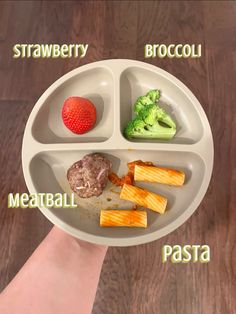 a person holding a plate with food on it and labeled in different languages, including broccoli, meatball, pasta