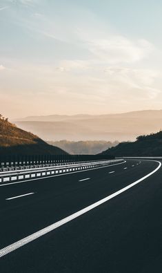 an empty highway with mountains in the background at sunset or sunrise, as seen from above