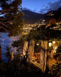 an outdoor area overlooking the water at night with lights on and people sitting in it