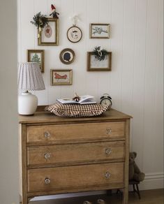 an old dresser with pictures on the wall above it and a lamp next to it