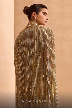 a woman wearing a gold dress with sequins on the shoulders and back, standing in front of a beige wall