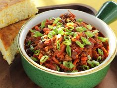 a green bowl filled with food next to a slice of bread on top of a table