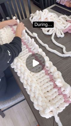 a person sitting at a table working on a knitted object with the words during