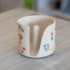 a white cup sitting on top of a table with flowers painted on the cups and sides