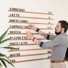 a man is writing on a wall with wooden letters and numbers in spanish, while another man holds his hand up to the sign