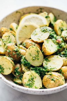 a white bowl filled with potatoes covered in herbs and garnished with lemon wedges