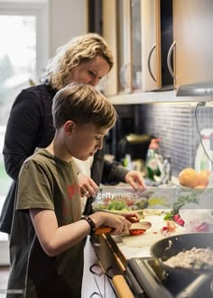 a woman helping a boy prepare food in the kitchen