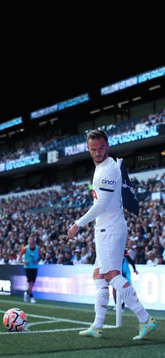 a man in white uniform kicking a soccer ball on field with people watching from the stands