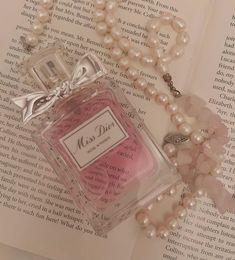 a bottle of perfume sitting on top of an open book next to pearls and a necklace